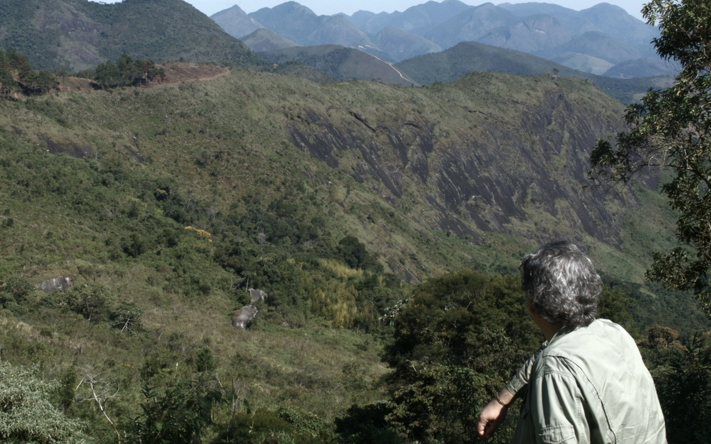 Homem de costas sentado observando a paisagem montanhosa.