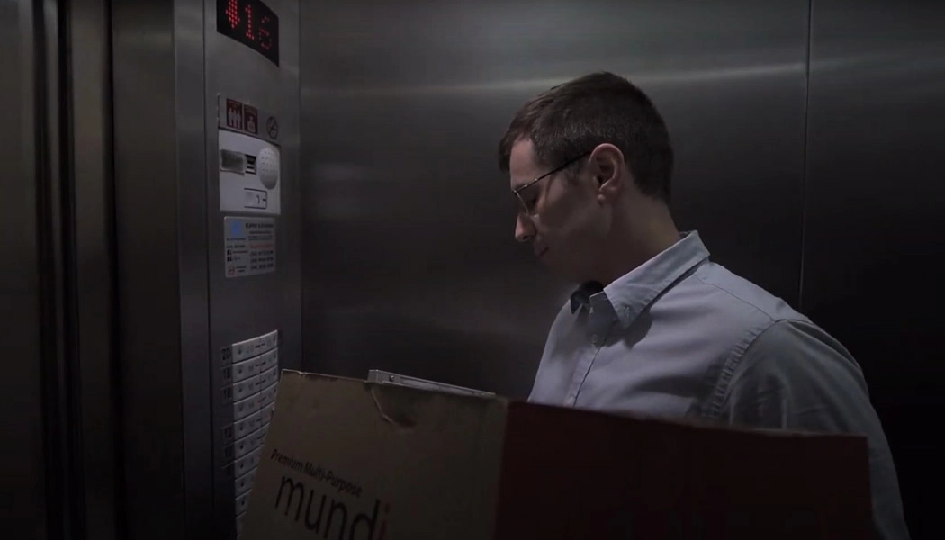 Homem dentro de elevador com caixa nos braos.