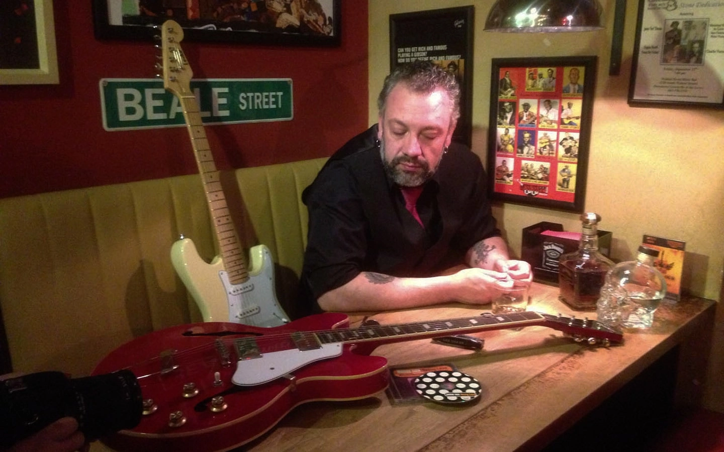 Cristian Rigon sentado em banco de bar com uma guitarra ao lado.