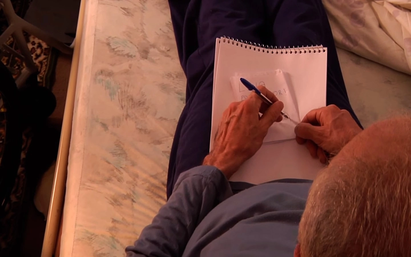 Pessoa sentada sobre cama com uma caneta e caderno em mos.