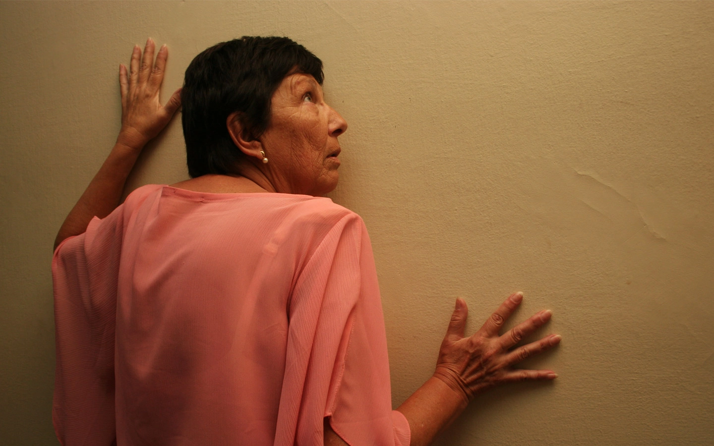 Mulher com o ouvido encostado em uma parede como se tentasse escutar algo.