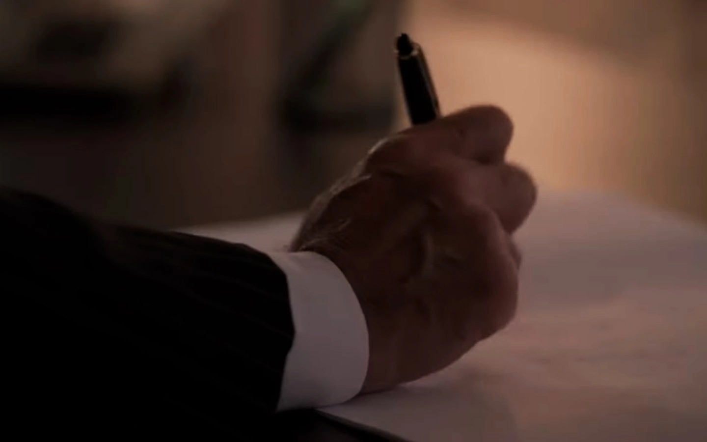 Mo de uma pessoa de terno escrevendo em um papel.