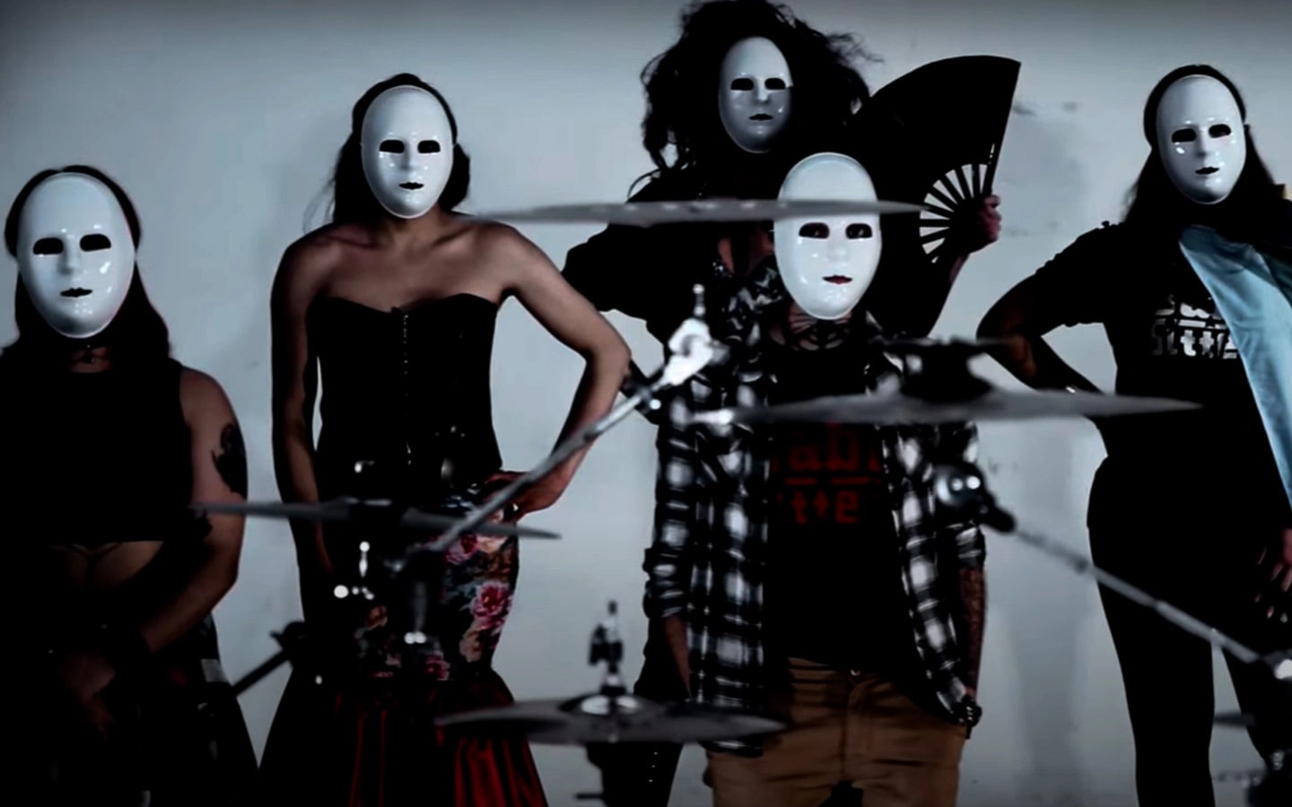 Cinco pessoas com mscara branca - um homem e quatro mulheres (uma delas com um leque na mo) - atrs de uma bateria.